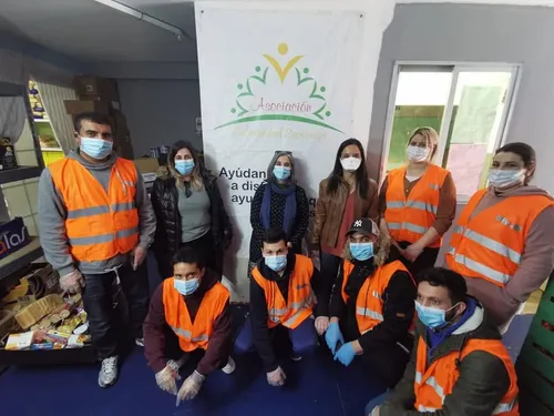 Equipo de voluntarios con mascarillas y chalecos naranjas junto al banner de la Asociación Solidaridad Esperanza en sus instalaciones de Getafe